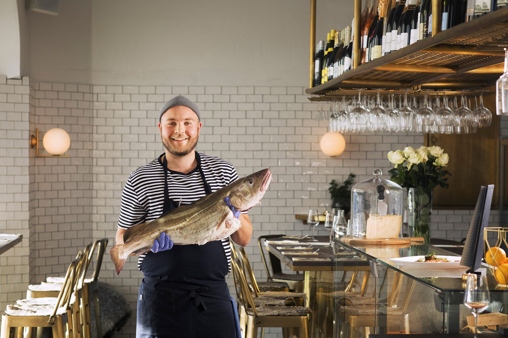 En glad man i personalen håller upp en stor fisk i restaurangen.
