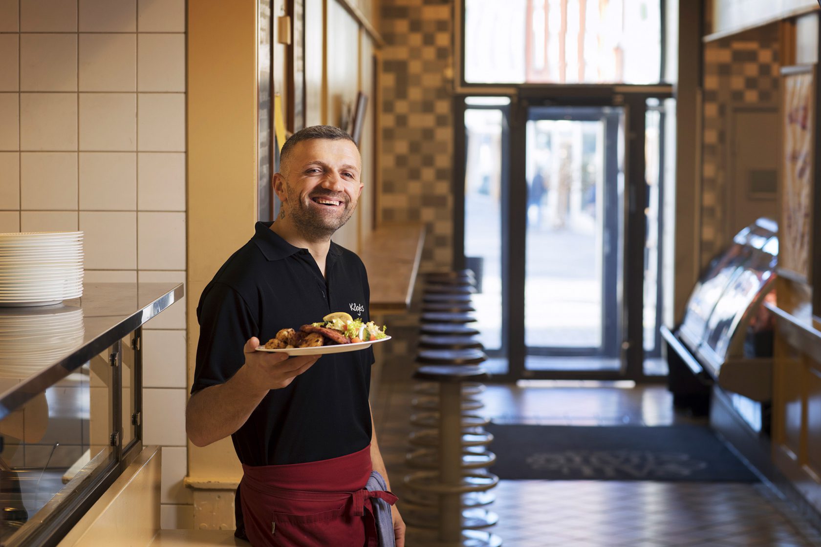 En man i personalen står med en tallrik mat framför restaurangen.