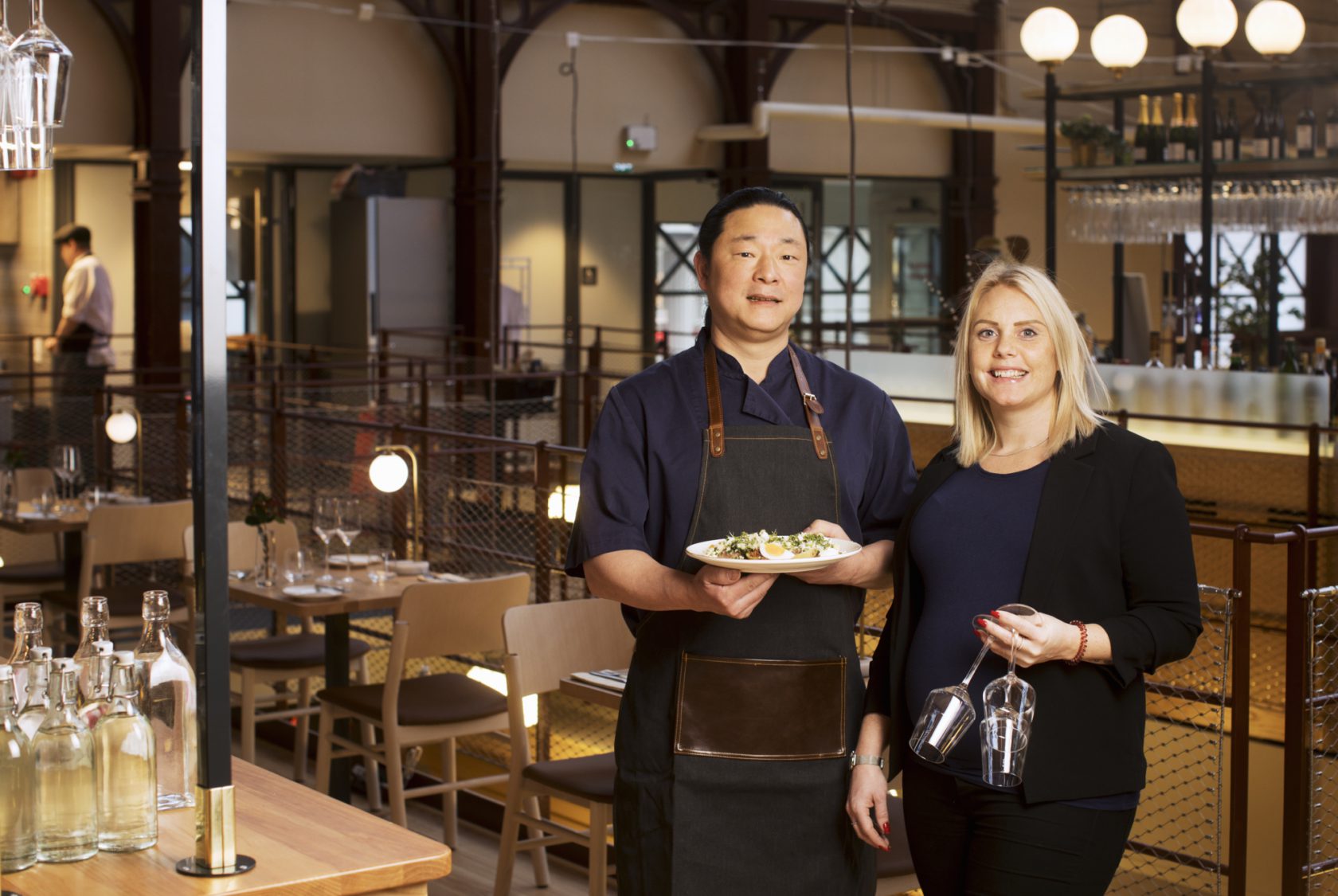 Restaurangpersonal står med en tallrik mat och två glas i handen.